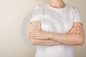 Cropped closeup photo of young woman in white t-shirt with crossed arms on  grey background with empty space