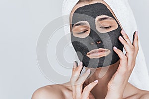 Cropped closeup portrait of beautiful young woman applying clay black mask, doing beauty wellness treatment on her face skin.