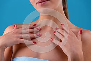 Cropped frontview of model touching her face and neck tenderly. Feminine hands with accurete nails on blue studio