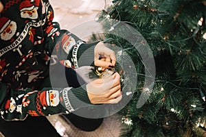 Cropped girl hang Christmas bal to a tree