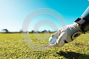 Cropped hand of african american young man wearing glove placing golf ball on tee against clear sky