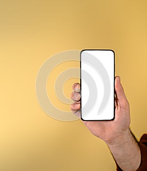 Cropped hand of businessman showing smart phone with blank white screen against beige background. Young male entrepreneur holding