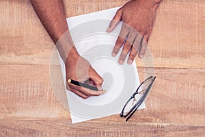 Cropped hand of businessman writing on paper by eye glasses at desk