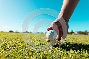 Cropped hand of caucasian young man placing golf ball on tee against clear blue sky on sunny day