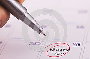 Cropped hand holding grey pen and word  UPCOMING EVENT written on calendar