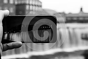 Cropped hand holding a mobile phone against waterfall