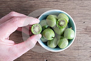 Cropped hand picking hardy kiwi fruit or kiwi berry from ceramic bowl on table