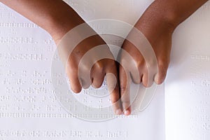 Cropped hands of african american elementary schoolgirl studying while touching braille book