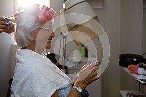 Cropped hands of hairstylist removing curlers from senior woman hair