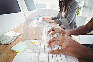 Cropped hands typing on keyboard at computer desk with coworker