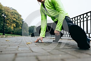 Cropped head image of sportsman stretching outdoor in the city lake background. Fitness male exercising in the park, wearing green