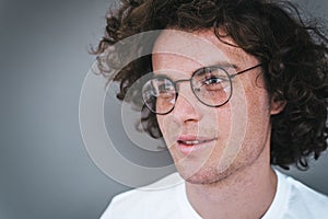 Cropped horizontal view portrait of handsome young male with curly hair, wearing white t-shirt and round trendy spectacles,