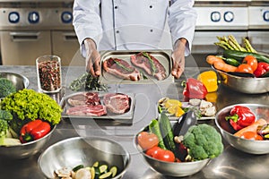 cropped image of african american chef holding tray with unprocessed meat at restaurant photo