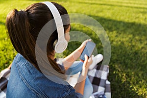 Beautiful young woman student in the park listening music with headphones using mobile phone.