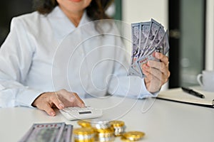 Cropped image, An Asian aged woman using calculator, holding US dollar banknotes