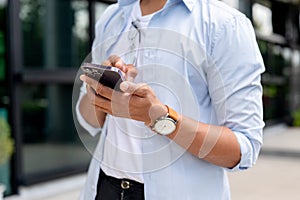 A cropped image of an Asian man in casual clothes is using his smartphone while walking in the city photo