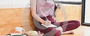 Cropped image of an Asian woman is taking notes while sitting on the wooden bench.