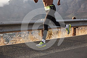 Cropped image of athlete runner runs on road, photographhed in motion, wears comfortable sneakers, takes part in