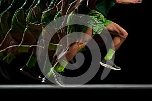 Cropped image of athletic, muscular male legs in motion, running against black background with stroboscope effect