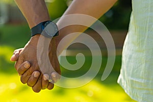 Cropped image of biracial senior man wearing wristwatch holding senior wife's hand in park