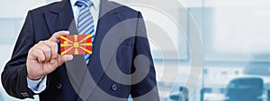 Cropped image of businessman holding plastic credit card with printed flag of North Macedonia. Background blurred