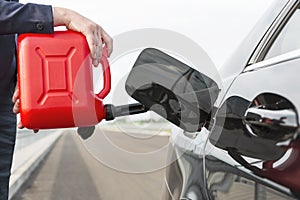 Cropped image of businesswoman with canister fueling car against sky