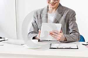 Cropped image of businesswoman in grey suit using tablet at table