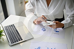 Cropped image of a businesswoman using calculator to calculate sales, working at her desk