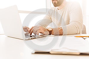 Cropped image of caucasian man 30s wearing wrist watch and casual clothing working on laptop, while sitting at table indoor