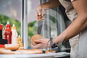 cropped image of chef cutting bun with knife in food truck