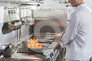 cropped image of chef frying steak with fire