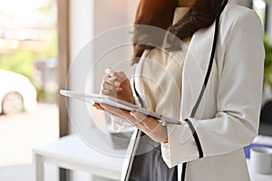 Cropped image of a confident Asian businesswoman using her tablet while standing in the office