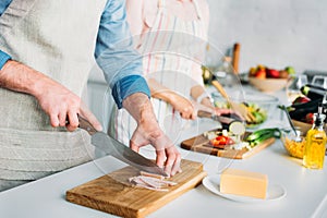 cropped image of couple cooking and cutting vegetables with meat