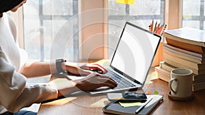 Cropped image of creative woman`s hands typing on computer laptop that putting on wooden working desk.