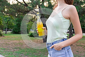 Cropped image of a cute girl who is having a walk in the park holding a bottle of orange juice in a sunny warm day