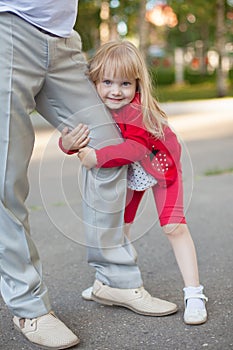 Cropped image of cute little girl looking at camera while hugging her father's leg not letting him go