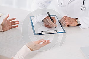 cropped image of doctor writing down something to clipboard