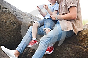 cropped image of father and son using smartphone on stones