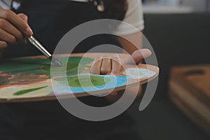 Cropped image of female artist standing in front of an easel and dipping brush into color palette