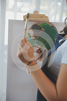 Cropped image of female artist standing in front of an easel and dipping brush into color palette