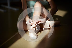 Cropped image of female ballerina legs, girl putting on pointe shoes. Model in ballet studio, school on daytime with