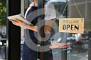 Cropped image, Female barista or coffee shop owner stands at her coffee shop`s entrance door