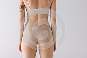 Cropped image of female body, back buttocks in beige underwear isolated over grey studio background. Medical care .