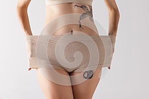 Cropped image of female body, belly and buttocks isolated over grey studio background. Elastic underwear
