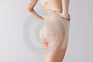 Cropped image of female body, buttocks in beige underwear isolated over grey studio background. Anti-cellulite care.