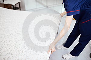 A female chambermaid making bed in hotel room