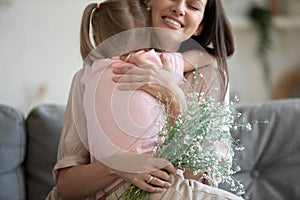 Cropped image focus on flowers, excited young mother cuddling daughter.