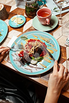 Cropped image a girl eating a meat dish in a restaurant with a fork and knife. Top view of girls hands and a plate. Lifestile phot