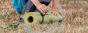 Cropped image of girl rolling yoga mat. Close-up of attractive young woman folding green yoga or fitness mat after working out in