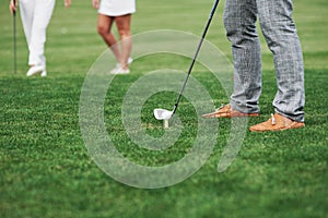 Cropped image of golfer who take aim for the shot. Two friends standing at background